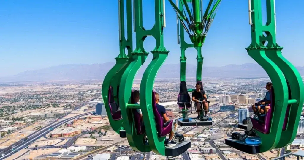 Thrill-seekers experience the excitement of a high-altitude ride on green amusement chairs overlooking the Las Vegas skyline, capturing the essence of adventure in the city.