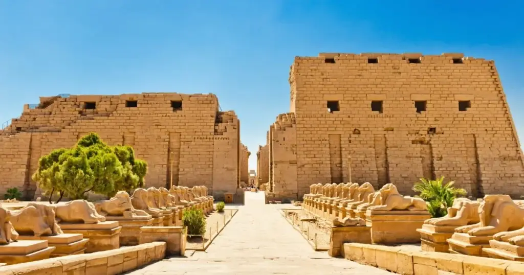 Pathway lined with sphinx statues leading to the entrance of the Karnak Temple in Luxor, spots in Egypt , with ancient stone walls under a clear blue sky.