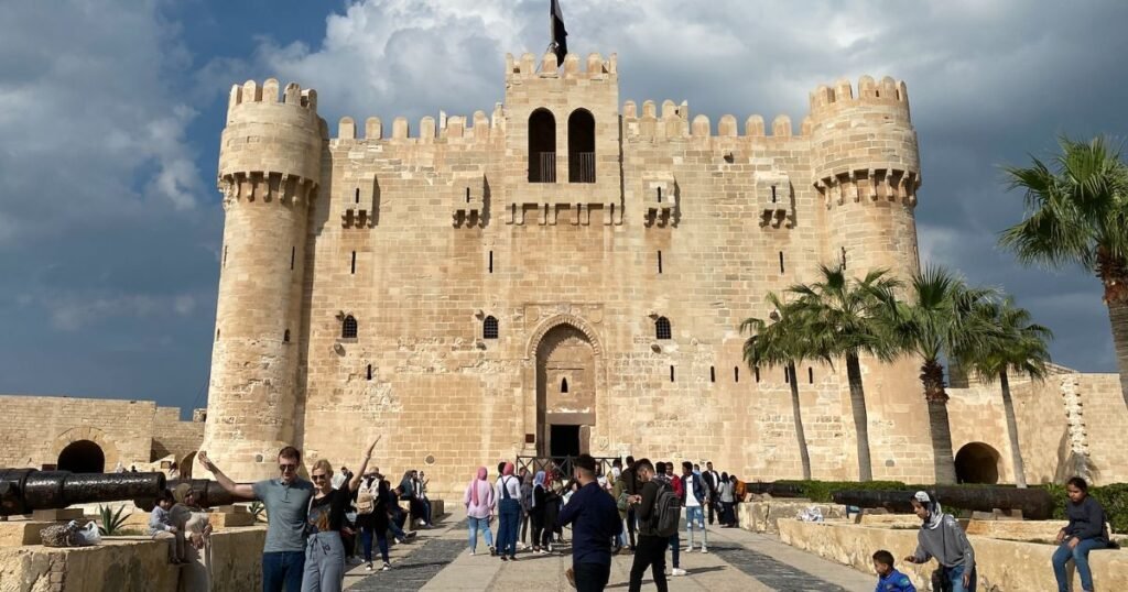 Alexandria's Citadel of Qaitbay with tourists visiting the historic fort, surrounded by palm trees and cloudy skies spots in Egypt 